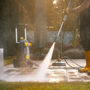 A Person Power Washing a Patio With a Pressure Washer in a Sunny Outdoor Setting A Person Power Washing a Patio With a Pressure Washer in a Sunny Outdoor Setting